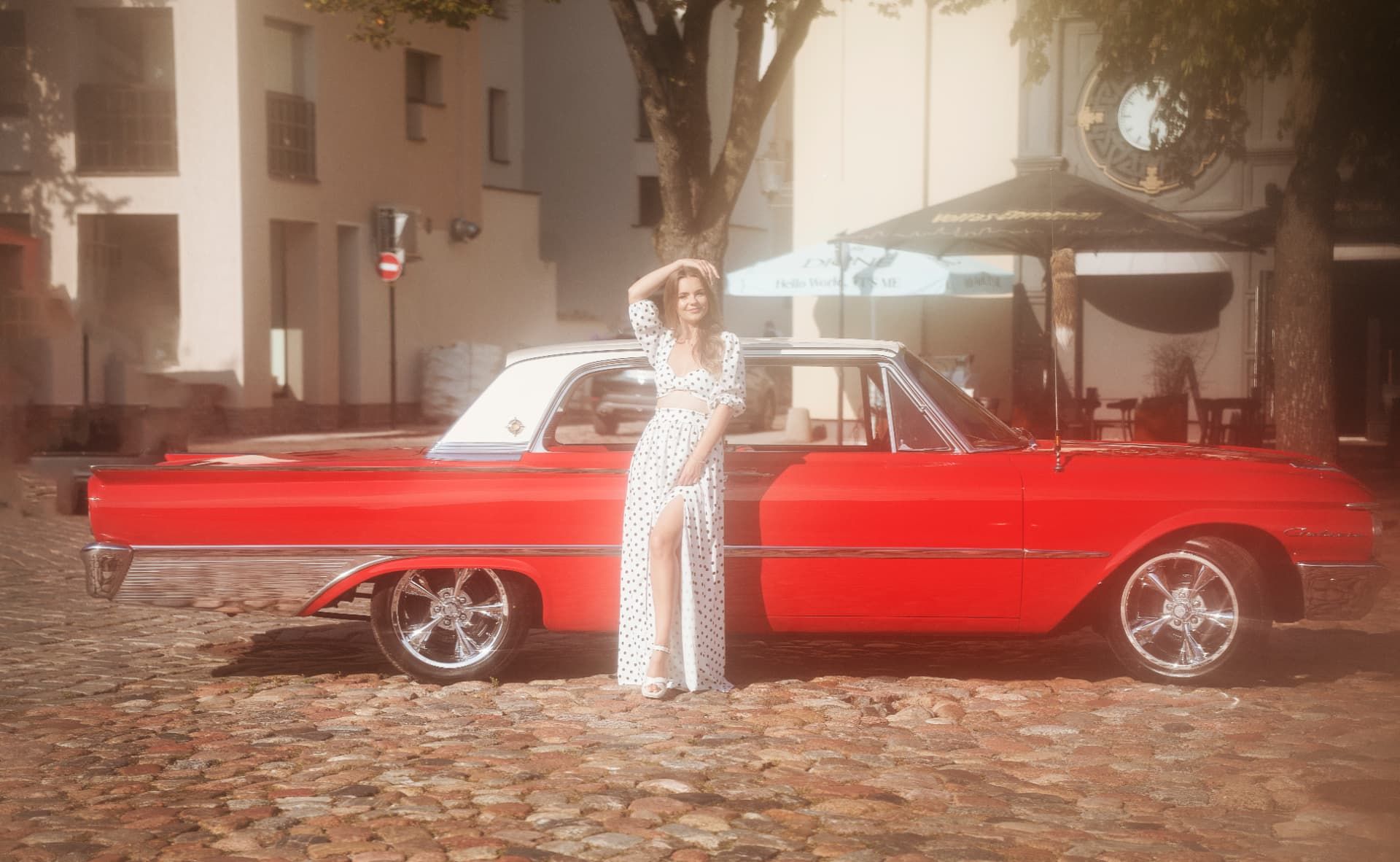 Ilgas raudonas Ford Galaxie šonas su baltu stogu ir chromo juostomis; šalia stovi modelis baltu drabužiu